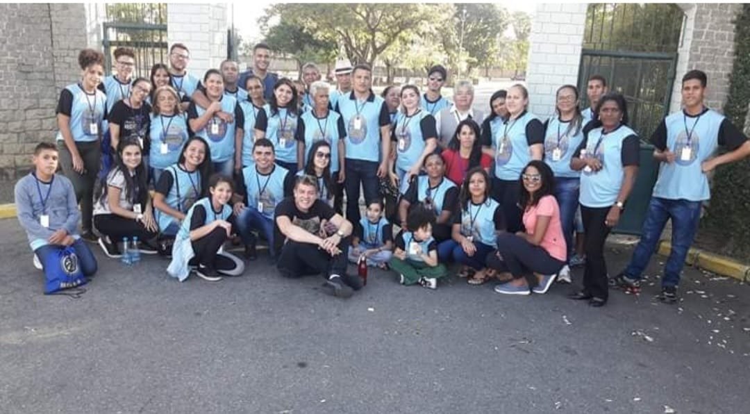 Grande grupo da caravana com camisetas azul-claro na entrada do acampamento